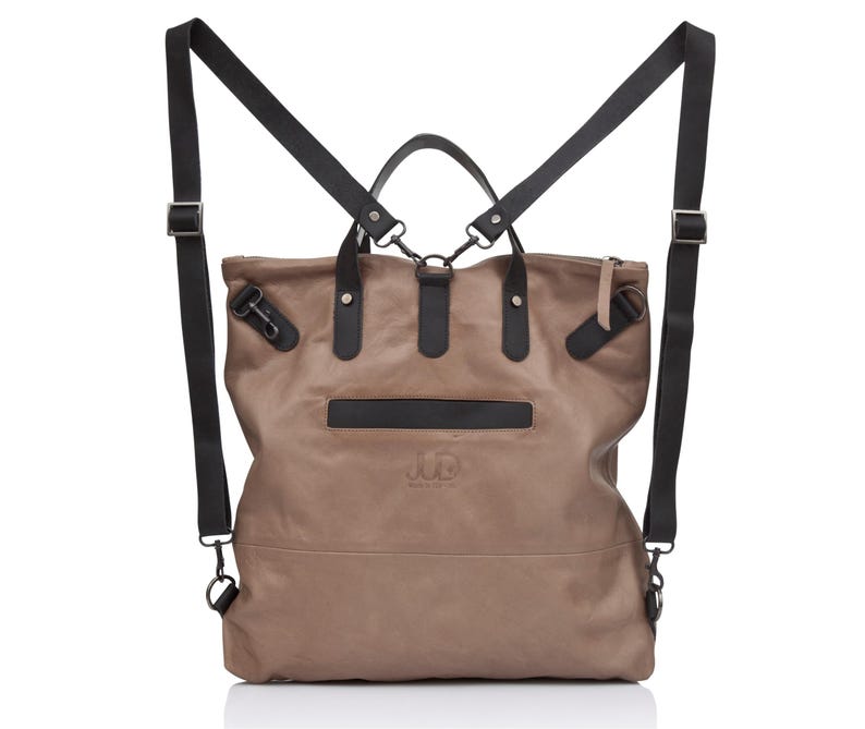 May include: A brown leather backpack with black straps and a front pocket. The bag has a logo on the front that says "J.D."