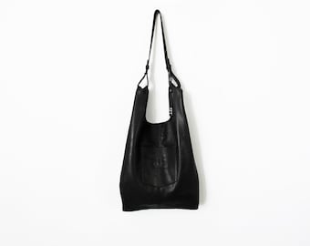May include: A black leather tote bag with a single strap and a large pocket on the front.