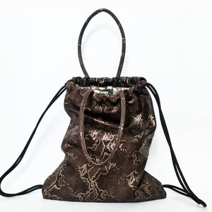 May include: A brown snakeskin-patterned drawstring bag with black straps and a top handle. The bag has a drawstring closure and a floral patterned lining.