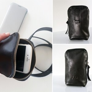 K&ouml;nnte beinhalten: Schwarze Leder-Handytasche mit Rei&szlig;verschluss und Trageriemen. Die Tasche ist mit einem Smartphone darin abgebildet.