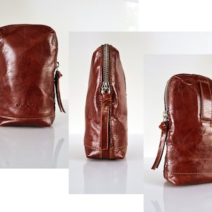 Könnte beinhalten: Eine braune Leder-Reißverschlusstasche mit einem silbernen Reißverschluss-Zipper. Die Tasche wird aus drei verschiedenen Blickwinkeln gezeigt.