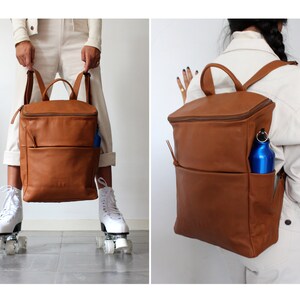 May include: A brown leather backpack with a zippered top and a front pocket. A blue water bottle is in the pocket. The backpack is being worn by a person.
