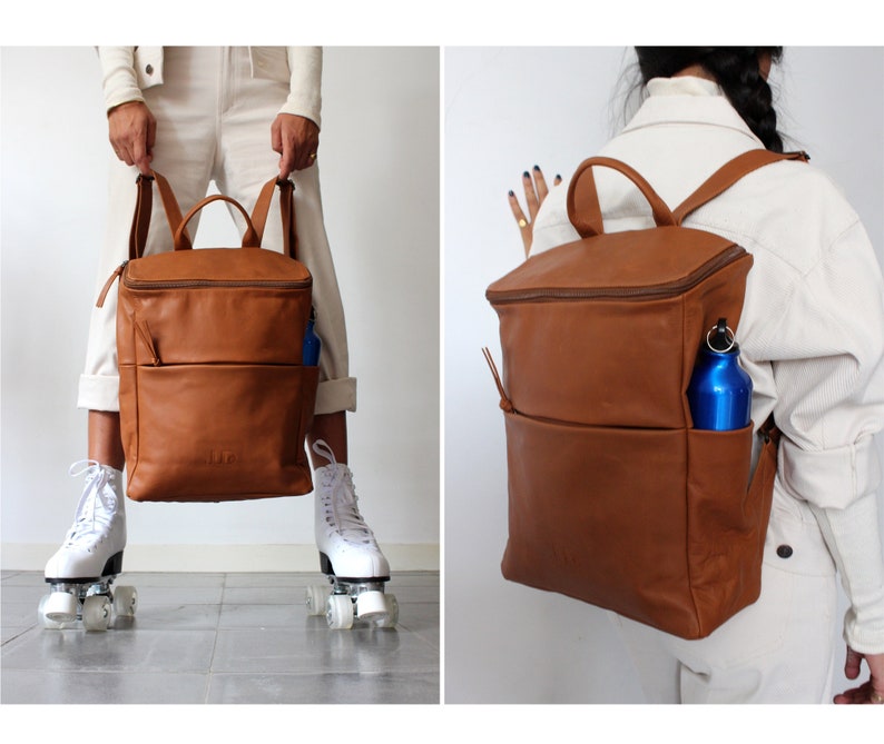 May include: A brown leather backpack with a zippered top and a front pocket. A blue water bottle is in the pocket. The backpack is being worn by a person.