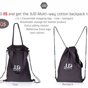 Op de afbeelding: Een zwarte katoenen tote bag met een trekkoord sluiting en verstelbare banden. De tas kan als rugzak of tote bag worden gedragen. De tas heeft een reflecterend logo met de tekst "JUD Made in TLV - IS".