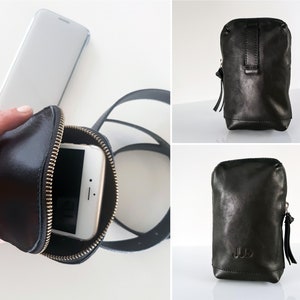 May include: Black leather phone case with a zipper closure and a strap. The case has a pocket for a phone and a small pocket on the front. The case is shown with a phone inside.