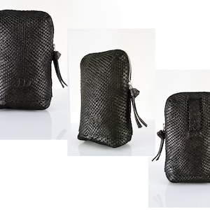 Puede incluir: Bolsa de cuero negro con cremallera y un patrón texturizado de piel de serpiente. La bolsa tiene un pequeño tirador de cremallera con un borla.