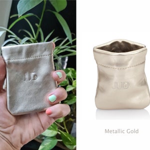 May include: A small, metallic gold pouch with a drawstring closure. The pouch has the letters "JUB" embossed on the front.