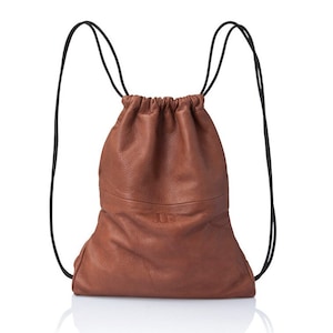 May include: A brown leather drawstring backpack with black drawstrings. The bag has a small, embossed logo on the front.