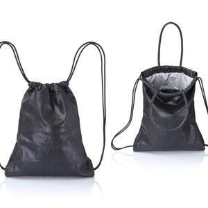 May include: A black leather drawstring bag with a top handle. The bag can be worn as a backpack or carried by hand.