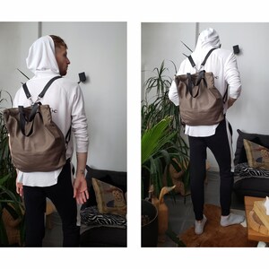 May include: A brown leather backpack with adjustable straps. The backpack has a large main compartment and a smaller front pocket. The backpack is being worn by a person.