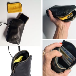 May include: A black leather phone pouch with a zipper closure. The pouch has a small pocket on the front and a larger pocket on the back. The pouch is shown with a phone, cards, and a small yellow leather pouch inside.