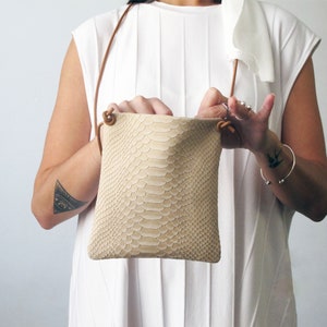 May include: A small, light beige snakeskin crossbody bag with a brown leather strap.