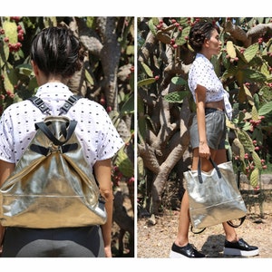 May include: Two views of a silver metallic leather backpack with black straps. The backpack is worn by a person in the first image and held by a person in the second image.