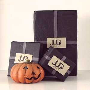 May include: Three black gift boxes with brown paper labels that say "JUD Made in Italy - NY - LA" and a small orange jack-o'-lantern.