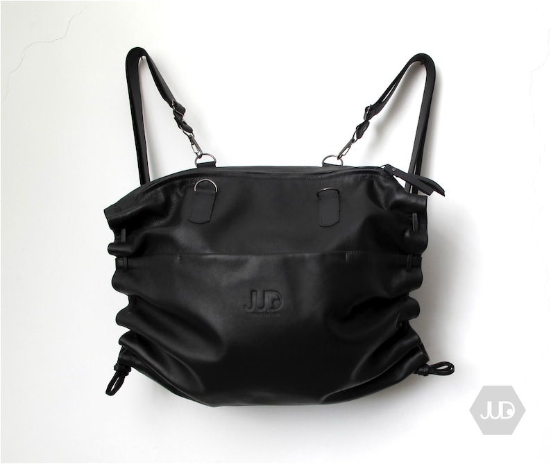 May include: Black leather backpack with adjustable straps and a drawstring closure. The bag has a  'JUD' logo embossed on the front.