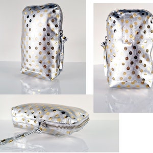 May include: A silver and gold polka dot makeup bag with a zipper closure and a tassel pull. The bag is laying flat on a white surface.