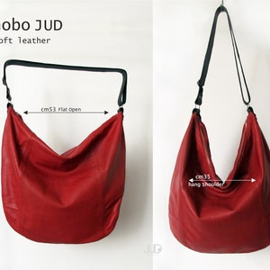 May include: Red leather hobo bag with a black adjustable strap. The bag measures 53 cm wide when laid flat and 42 cm tall. The strap is 35 cm long when hanging on the shoulder.