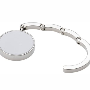 May include: A silver-toned, round, retractable keychain with a smooth, white surface. The keychain is designed to clip onto bags, purses, or belts.