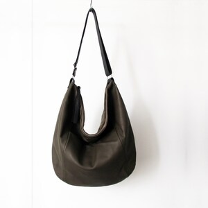 May include: A large, dark green leather tote bag with a black shoulder strap. The bag has a slouchy, casual look.