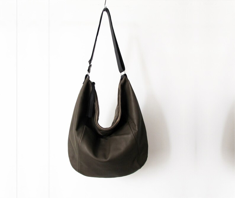 May include: A large, dark green leather tote bag with a black shoulder strap. The bag has a slouchy, casual look.