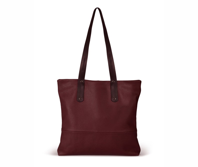 May include: A burgundy leather tote bag with black leather handles. The bag has a simple design and a spacious interior.