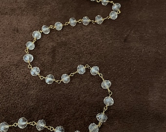 May include: A strand of clear faceted glass beads strung on gold wire. The beads are small and round, and the wire is thin. The strand is coiled up on a spool.