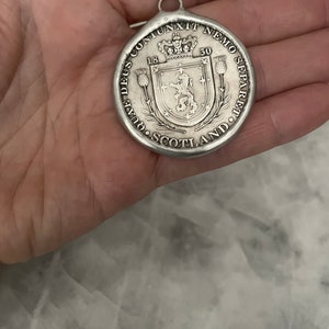 May include: A silver pendant with a lion and a crown on a shield. The pendant has the text "DEUS CONJUNXIT NEMO SEPARARE" and "SCOTLAND" around the edge. The pendant also has the dates "18" and "50" on it.