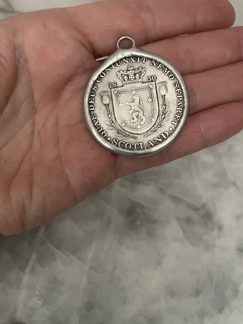 May include: A silver pendant with a lion and a crown on a shield. The pendant has the text "DEUS CONJUNXIT NEMO SEPARARE" and "SCOTLAND" around the edge. The pendant also has the dates "18" and "50" on it.