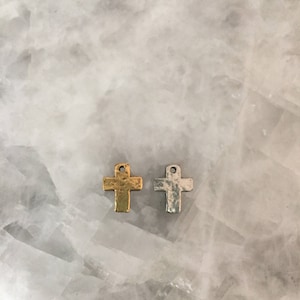 May include: Two small metal cross charms, one gold and one silver, on a white background.