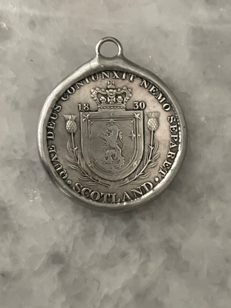 May include: Silver pendant featuring the Scottish coat of arms with a lion rampant, surrounded by the text "NEMO ME IMPUNE LACESSIT" and "1830", with the words "DUAL DEUS CONJUNXIT NEMO SEPARE" and "SCOTLAND" around the edge.