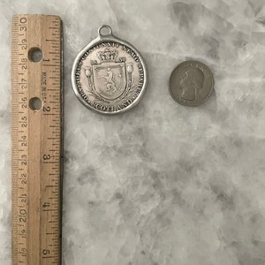 May include: Silver pendant with a Scottish coat of arms and the text "DEUS CONIUNXIT NEMO SEPARET" and "SCOTLAND" around the edge. The pendant is 1.5 inches in diameter.