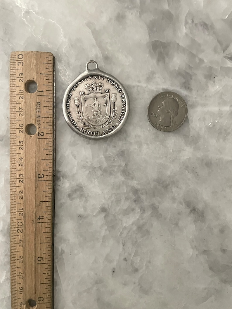 May include: Silver pendant with a Scottish coat of arms and the text "DEUS CONIUNXIT NEMO SEPARET" and "SCOTLAND" around the edge. The pendant is 1.5 inches in diameter.