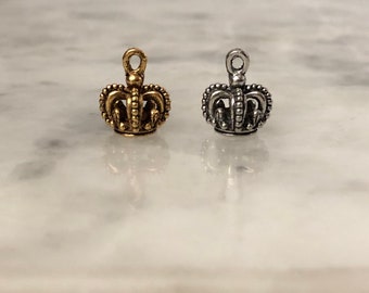 Puede incluir: Dos pequeños abalorios con forma de corona, uno dorado y otro plateado, con un bucle en la parte superior para sujetarlos a joyas u otras manualidades.