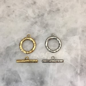 May include: Two hammered metal toggle clasps, one gold and one silver, with matching round rings.