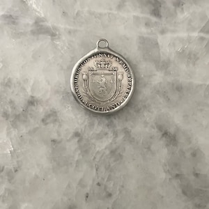 May include: Silver pendant with a Scottish coat of arms featuring a lion and a crown. The text around the coat of arms reads "NEMO ME IMPUNE LACESSIT" and "1530".