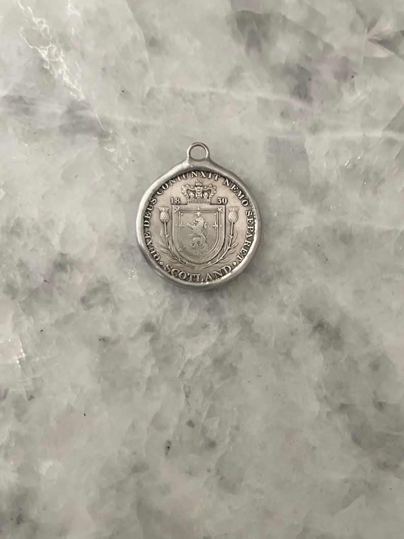 May include: Silver pendant with a Scottish coat of arms featuring a lion and a crown. The text around the coat of arms reads "NEMO ME IMPUNE LACESSIT" and "1530".