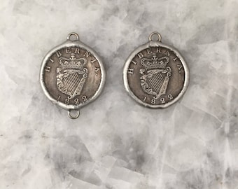 May include: Two silver-toned pendants featuring a harp and crown design. The pendants are inscribed with "HIBERNIA" and "1822".