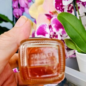Puede incluir: Un frasco de perfume cuadrado de vidrio con esquinas redondeadas que contiene un l&iacute;quido de color &aacute;mbar. La base del frasco presenta el texto CHANEL en relieve. El vidrio es transparente con un fondo grueso, mostrando el tono c&aacute;lido.