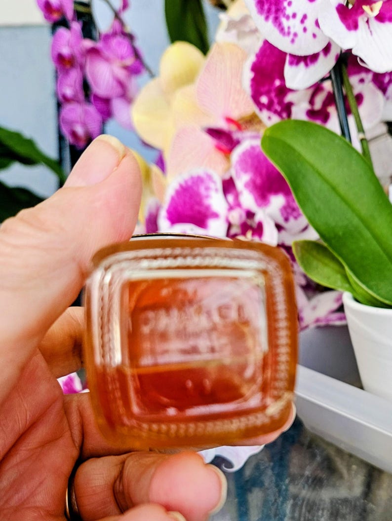Puede incluir: Un frasco de perfume cuadrado de vidrio con esquinas redondeadas que contiene un l&iacute;quido de color &aacute;mbar. La base del frasco presenta el texto CHANEL en relieve. El vidrio es transparente con un fondo grueso, mostrando el tono c&aacute;lido.