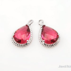 May include: A pair of silver teardrop earrings with red crystal accents. The earrings have a delicate, ornate design.