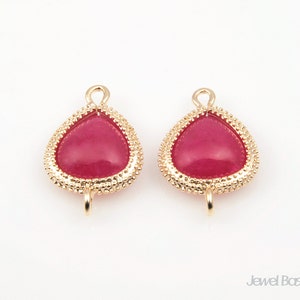 May include: A pair of gold-tone earring findings with a teardrop-shaped red glass stone.