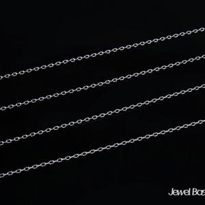 May include: Four silver chains laid out in parallel lines on a black background. The chains are made of small, linked oval shapes.