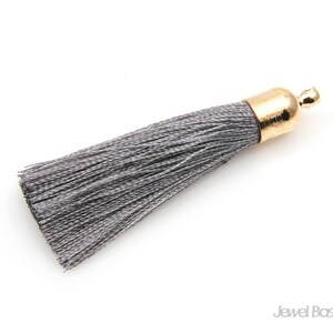 May include: A gray tassel with a gold metal top. The tassel is made of soft, silky threads.