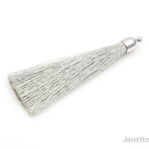 May include: A silver tassel with a metallic silver cap. The tassel is made of thin, shiny threads.