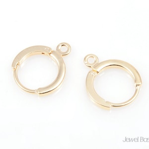 Puede incluir: Dos aros de pendientes de color dorado con un pequeño bucle en la parte superior. Los aros son lisos y tienen un acabado pulido.