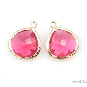 Può includere: Due ciondoli dorati a forma di goccia con inserti in vetro rosa. I ciondoli hanno una finitura dorata testurizzata.