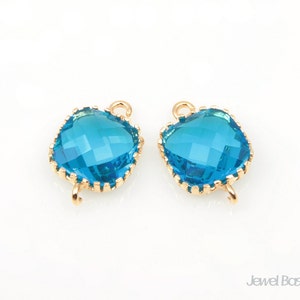 May include: Two gold-toned metal connector charms with a blue faceted glass square in the centre. The charms have a loop on each side for attaching to jewellery.