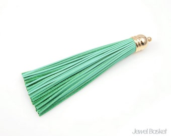 May include: A green leather tassel with a gold metal top. The tassel is made of many thin strands of leather.