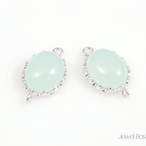 May include: Two silver-toned oval-shaped pendant charms with a light green cabochon stone in the center. The charms have a scalloped edge and a loop at the top.