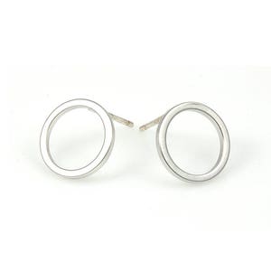 以下が含まれることがあります： シルバーの円形スタッドピアスのペア。ピアスはシンプルでミニマルなデザインで、滑らかで磨かれた仕上げになっています。